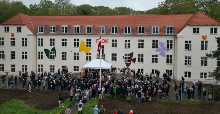 Dronefoto af FLOK med facadeudsmykning, flaget hejst og flere hundrede mennesker foran bygningen.